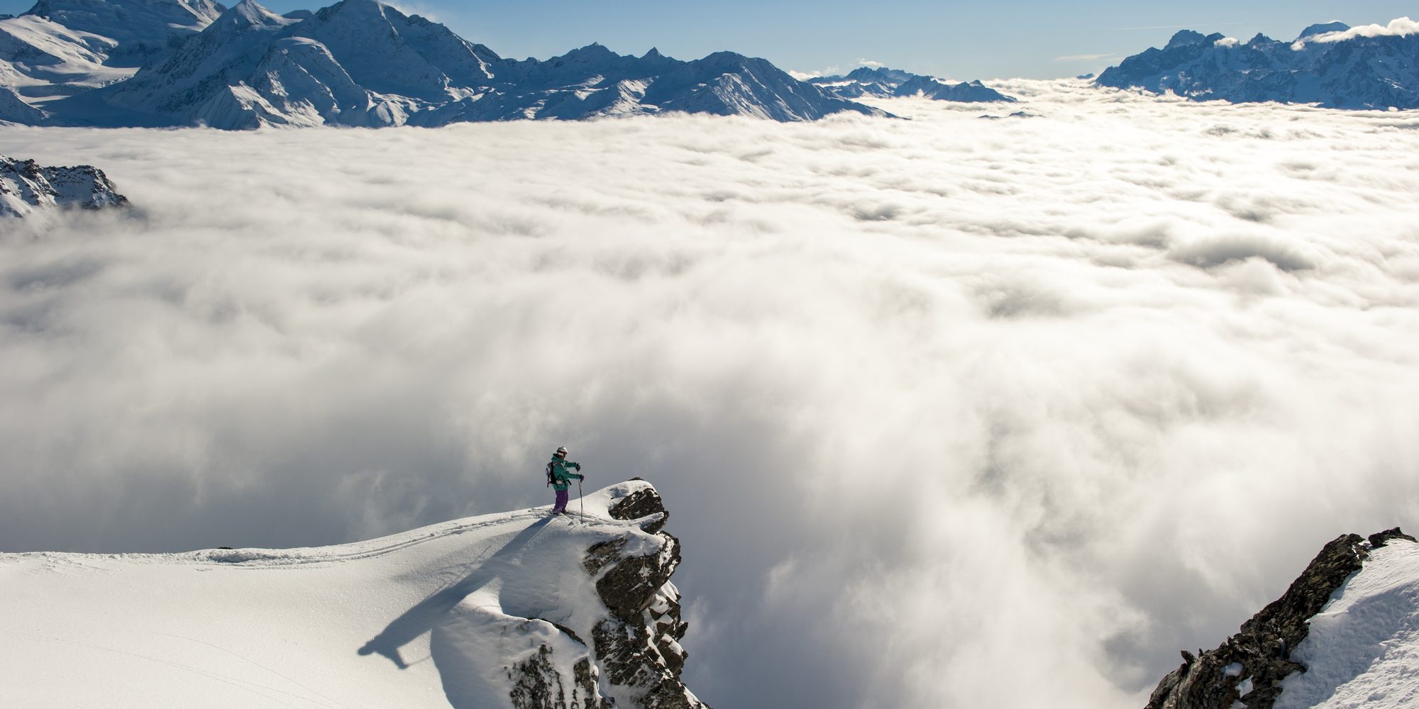A skier on a high ridge with the valley under cloud far below